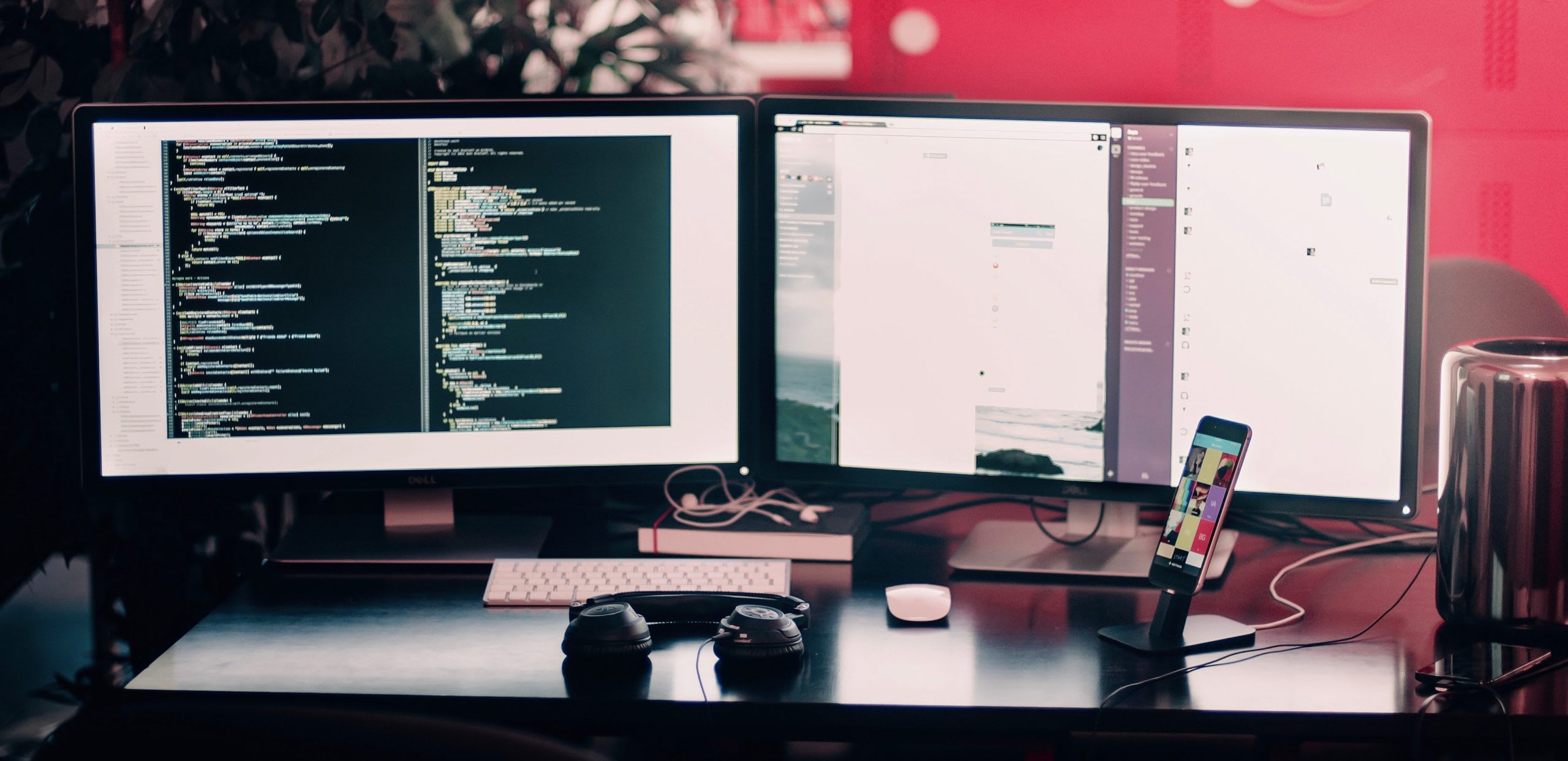 Coding work on a dual-monitor setup on a desk with headphones and cell phone.